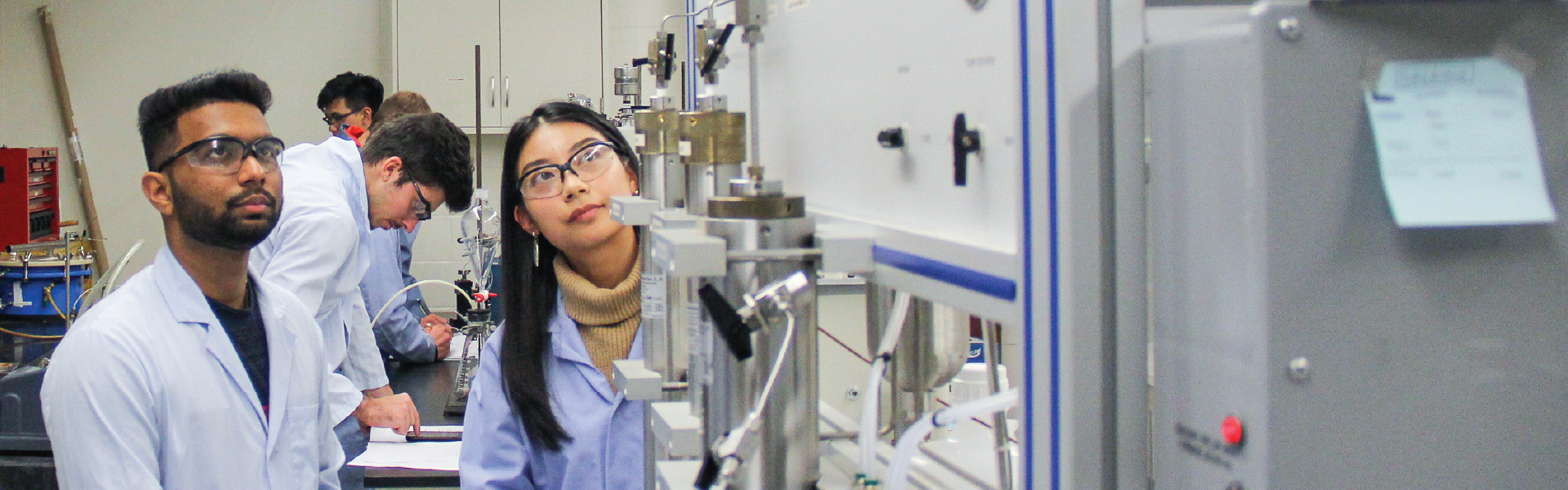 Students in lab coats conducting experiment in petrophysics lab.