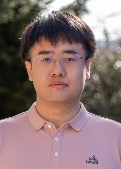 Guorui Sun wearing glasses and a light peach polo shirt with a blurred natural background.