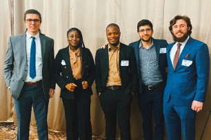 Graduate students in business attire in front of golden curtain backdrop.