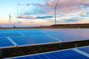 Solar panels in the foreground and wind turbines in the background under a colorful sky.