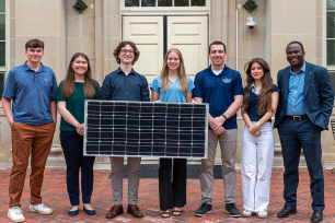 Group of students holding solar panel in front of Housler building.