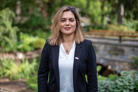 Elham Rahimi in a floral blouse stands in a lush garden with hydrangeas and greenery.