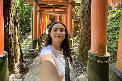 Sofia Hoffman taking a selfie while standing in a pathway lined with iconic red torii gates.