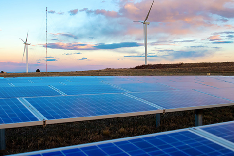 Solar panels in the foreground and wind turbines in the background under a colorful sky.