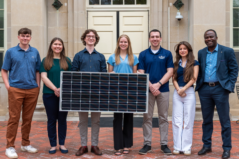 Group of students holding solar panel in front of Housler building.