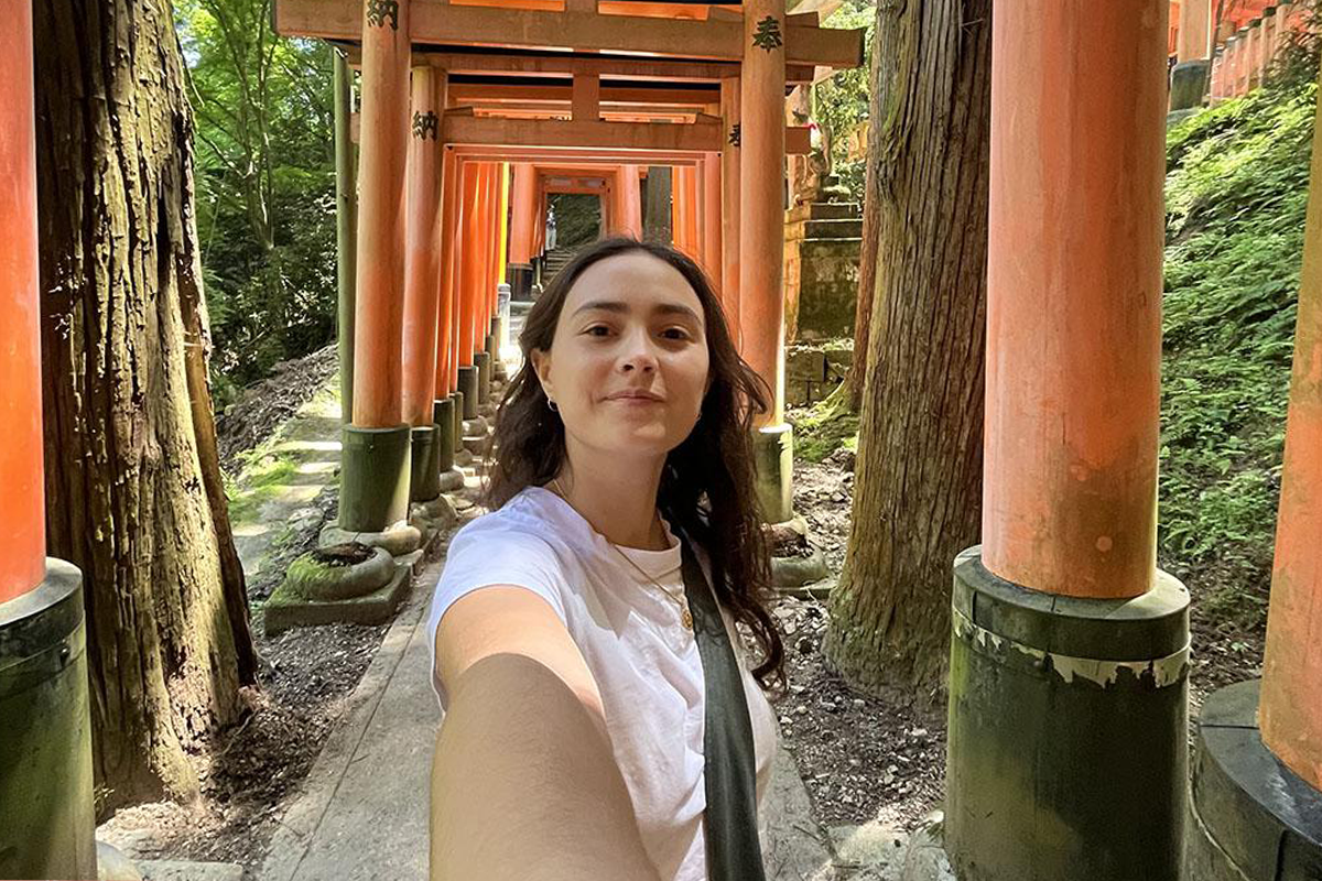 Sofia Hoffman taking a selfie while standing in a pathway lined with iconic red torii gates.