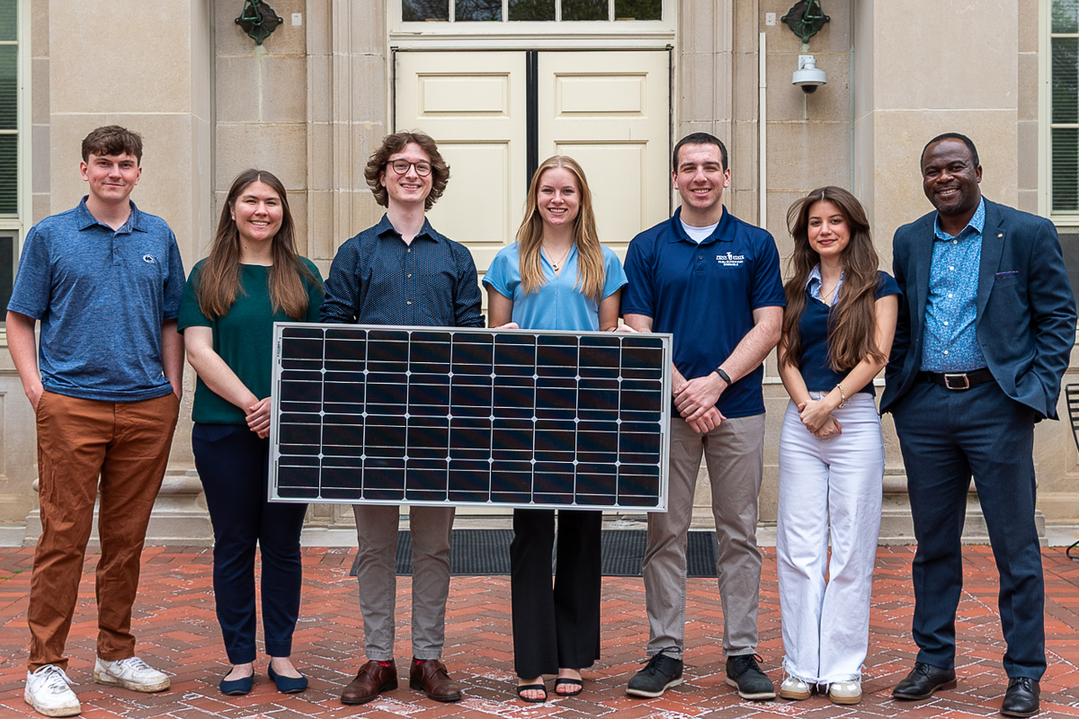 Group of students holding solar panel in front of Housler building.