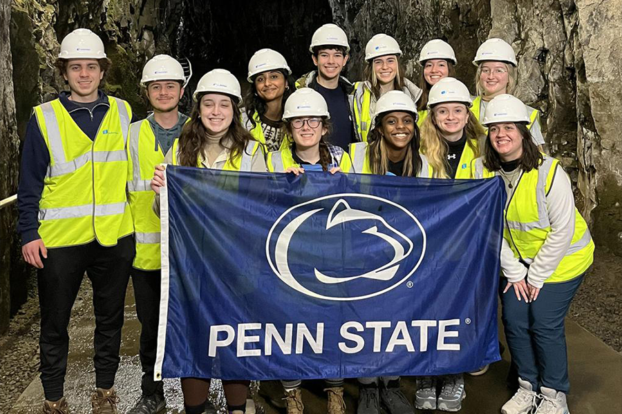 Student group in hardhats and safety vest hold Penn State Athletics flag in hydropower plant